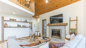 Un ampio soggiorno con soffitto alto, travi in legno, camino, televisore e un’accogliente zona relax.