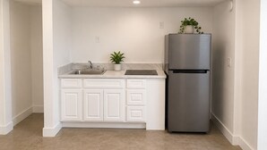 Cocina con armarios blancos, refrigerador de acero inoxidable, un lavamanos y una planta en maceta.