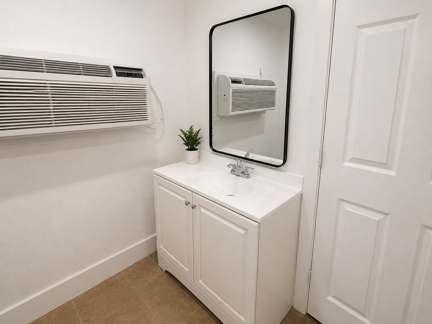 A bathroom with a white sink, a mirror, a potted plant, and a window with blinds.