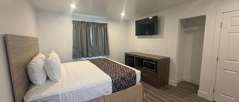 A bedroom with a bed, a TV, a wardrobe, and a door.