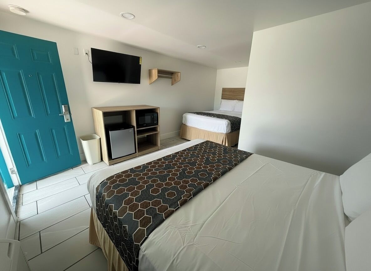 A hotel room with a bed, a television mounted on the wall, a wooden cabinet, and a teal door.