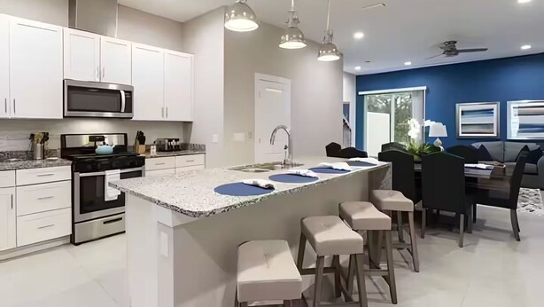 A modern kitchen with white cabinets, a microwave, and a stove. There is a bar area with stools and a dining table. - Gated Resort Home, Pool & Hot Tub Near Disney (Kissimmee)