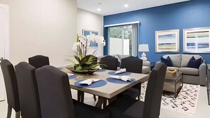 A modern living room with a dining area, a ceiling fan, and artwork on the walls. - Gated Resort Home, Pool & Hot Tub Near Disney (Kissimmee)