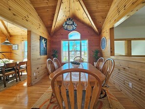 Ein Holzinterieur mit Esstisch, Stühlen, einer Chandelieber und einem großen Fenster.