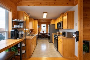 A compact kitchen with wooden cabinets, a refrigerator, microwave, and a coffee machine. - 270° Stunning Ocean View & 4 Private Epic Gardens! (Terence Bay)