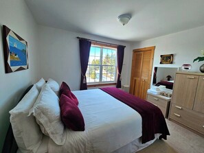 A bedroom with a bed, a window with curtains, a wardrobe, and a wall-mounted picture. - 270° Stunning Ocean View & 4 Private Epic Gardens! (Terence Bay)