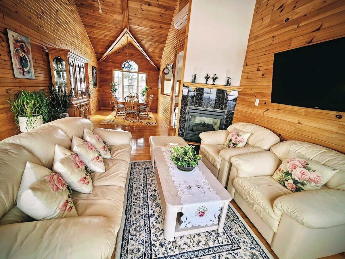 A log cabin interior with a fireplace, leather sofas, a coffee table, and a television.