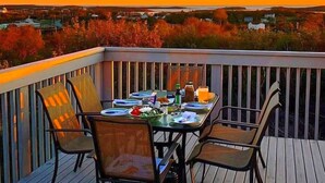 A deck with a table set for four, overlooking a landscape with trees and buildings. - 270° Stunning Ocean View & 4 Private Epic Gardens! (Terence Bay)