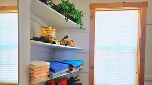 A storage unit with shelves containing folded towels, a plant, and a fruit basket. - 270° Stunning Ocean View & 4 Private Epic Gardens! (Terence Bay)