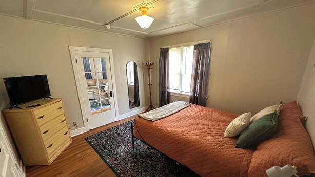 Un dormitorio con cama, cómoda, televisor y ventana con cortinas.