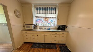 Una cocina compacta con microondas, lavamanos y una ventana con cortina decorativa.
