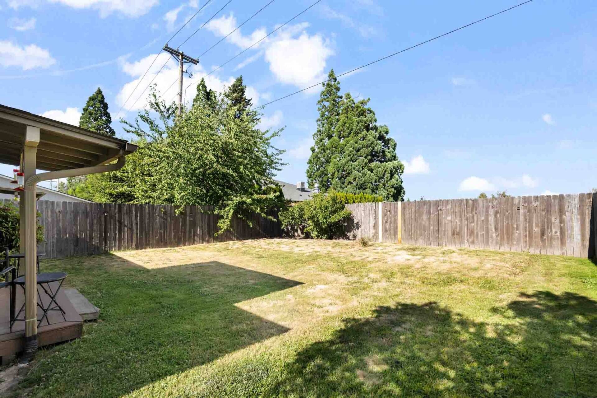 A backyard with a wooden fence, a covered patio area, and a grassy lawn.