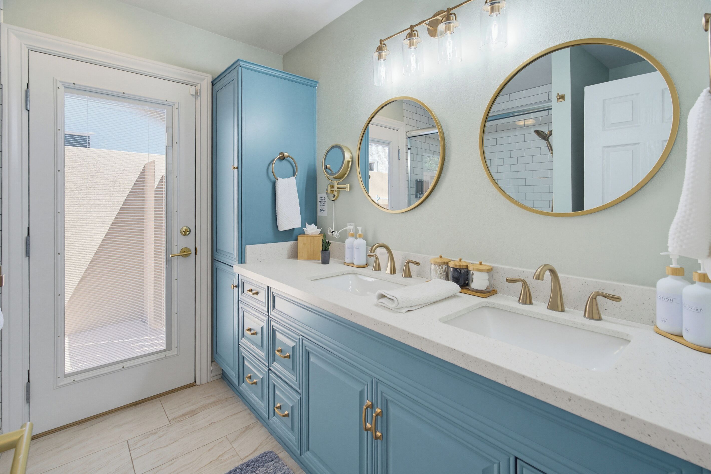 A bathroom with a white sink, gold faucets, a blue cabinet, and two round mirrors.