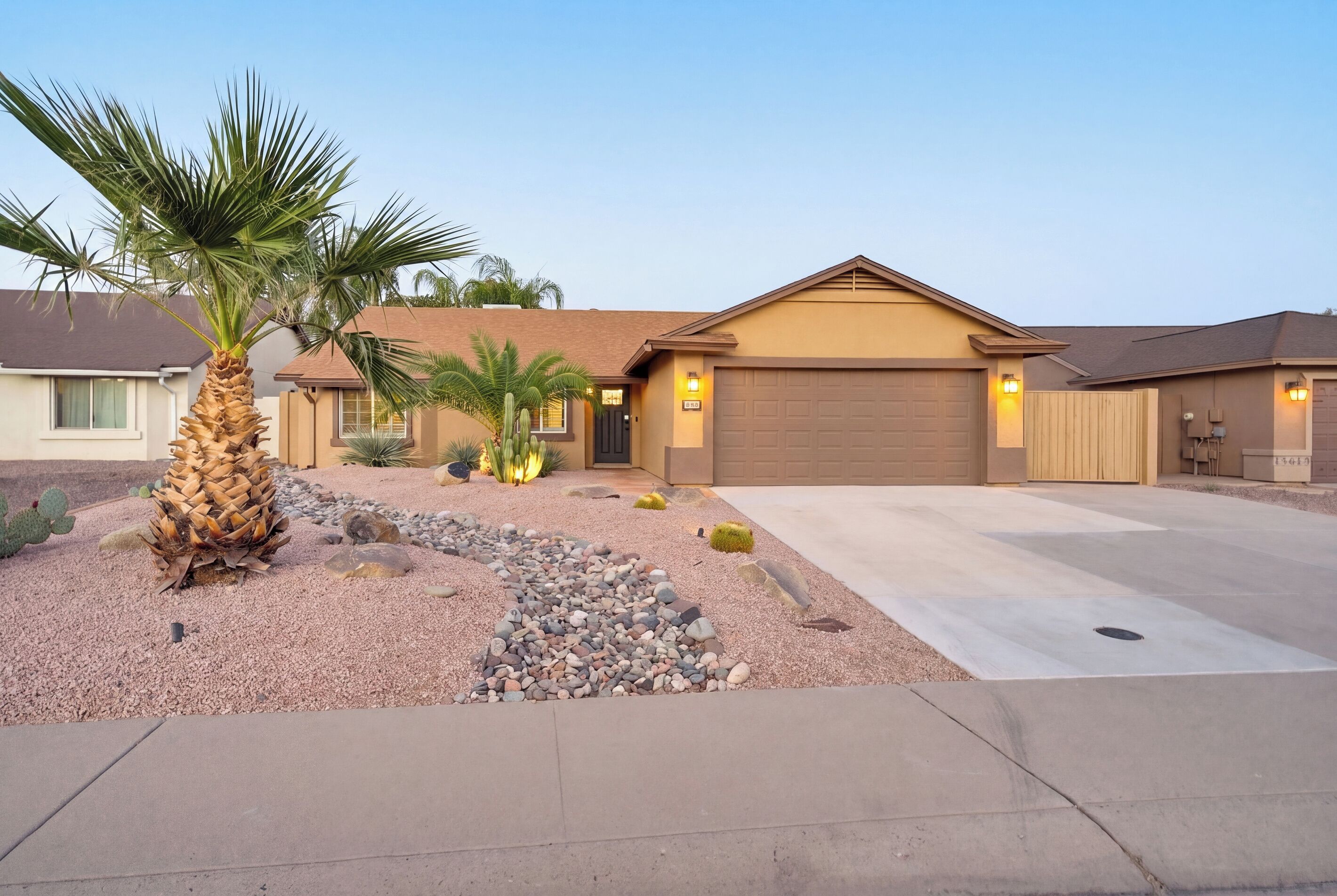 Una casa residenziale con garage, vialetto e giardino curato con una palma e alcuni cactus.