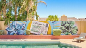 Ein Poolbereich mit Wandgemälde, Liegestuhl und einem Schild mit der Aufschrift 'Greetings from the Desert Belle'.