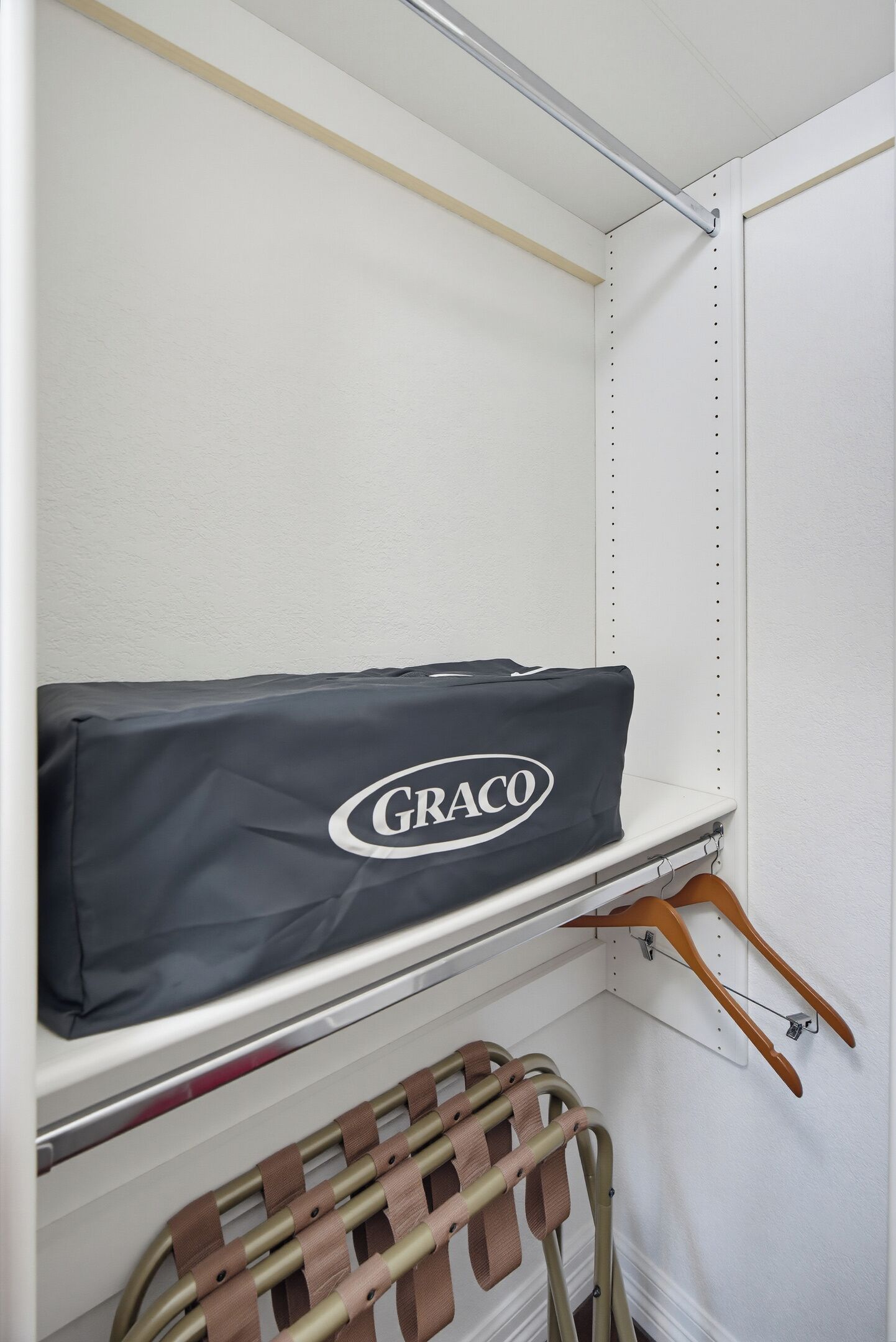 Ein Stauraum mit Regalen, einer Kleiderstange und einem Koffer mit dem Aufdruck 'GRACO'.