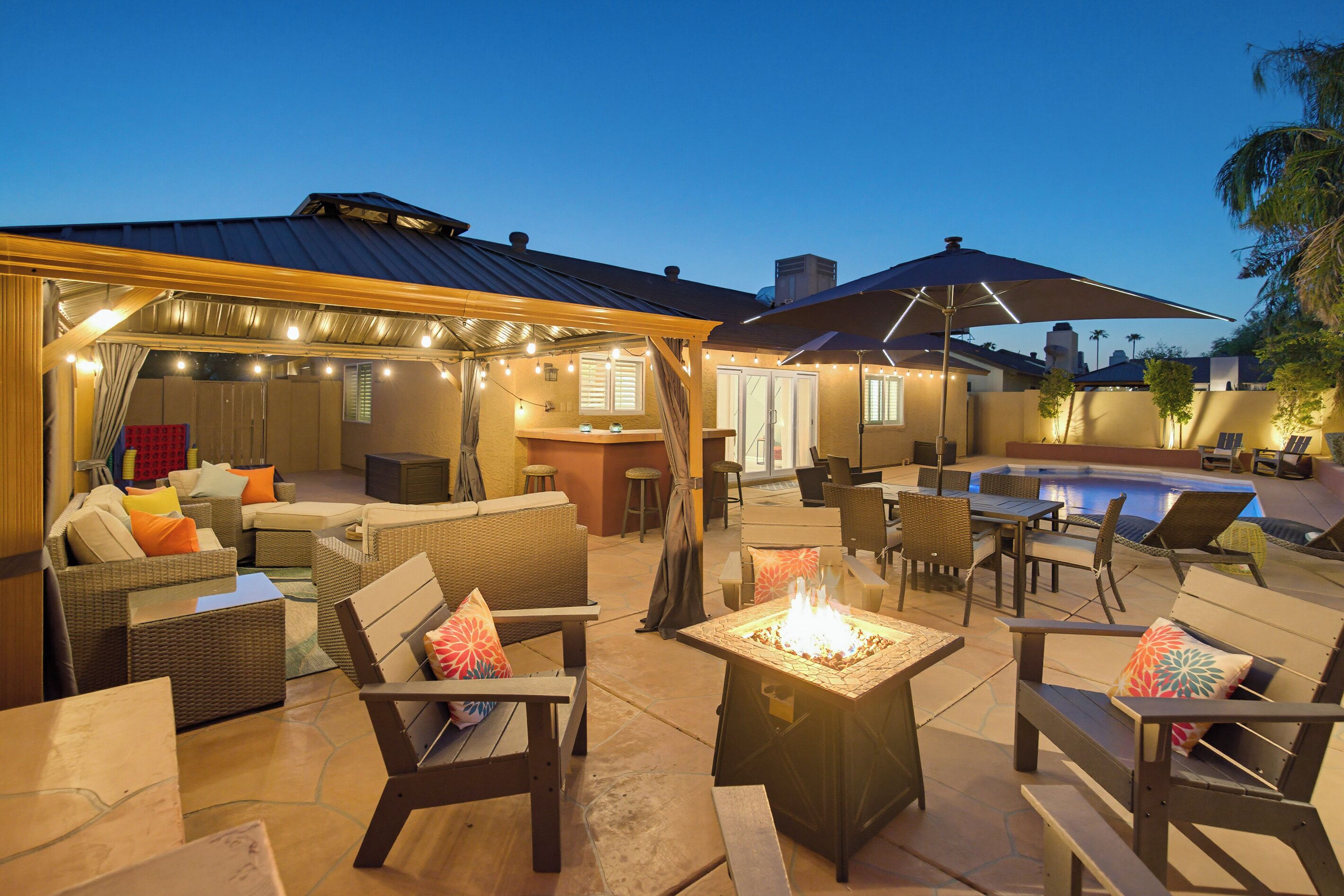 Un espace extérieur aménagé avec une terrasse, des sièges, une piscine et des guirlandes lumineuses.