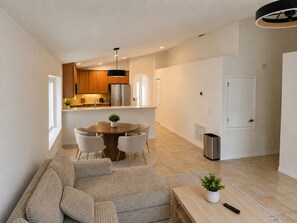A modern living room with a sofa, a dining table with chairs, a kitchen area with wooden cabinets and a refrigerator, and a white door. - Davenport Pool Home 4BR, Games Room, Minutes to Disney Parks (Davenport)