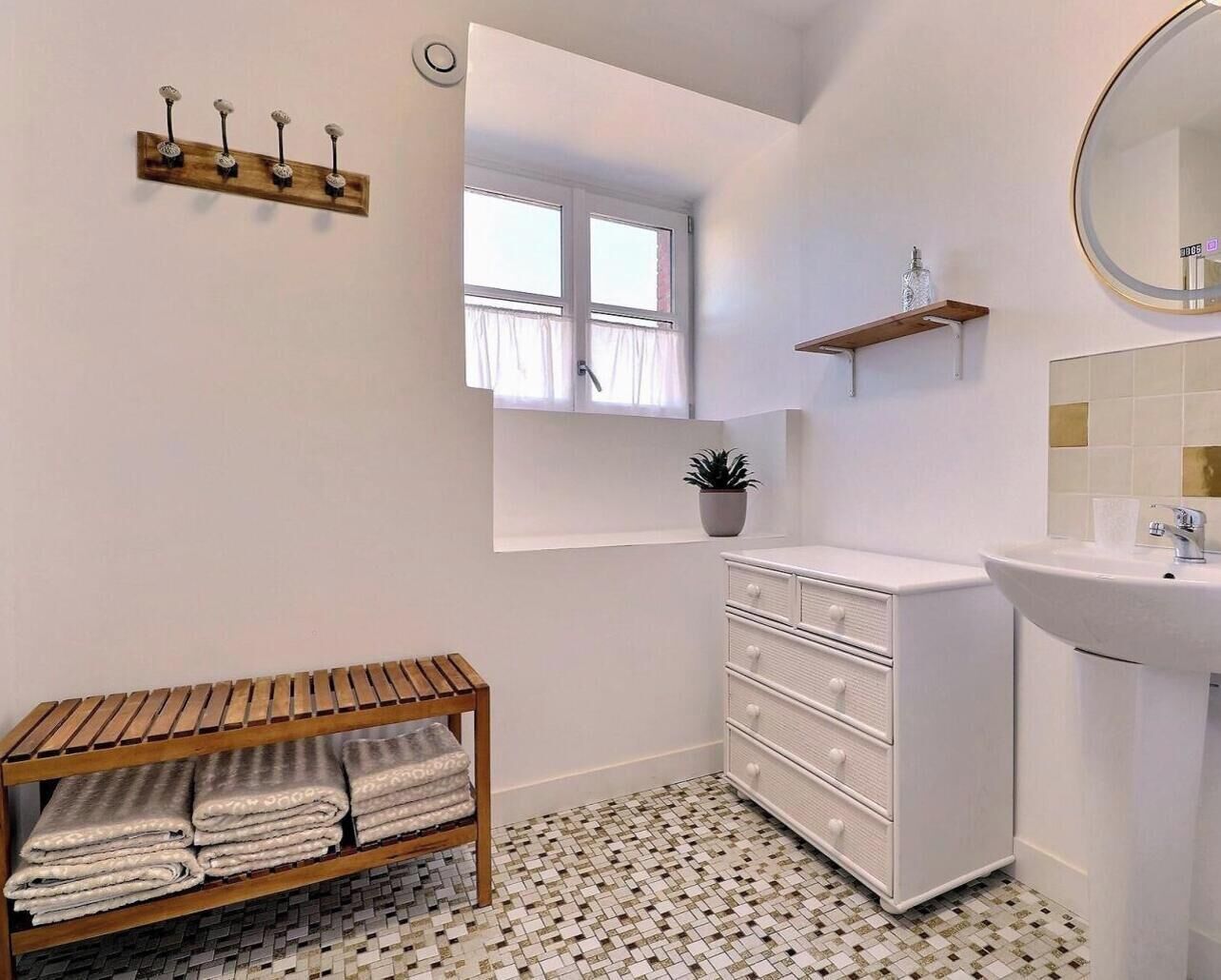 Ein Badezimmer mit einem weißen Waschbecken, einer hölzernen Ablage mit Handtüchern, einer Topfpflanze und einem Fenster mit Vorhängen.