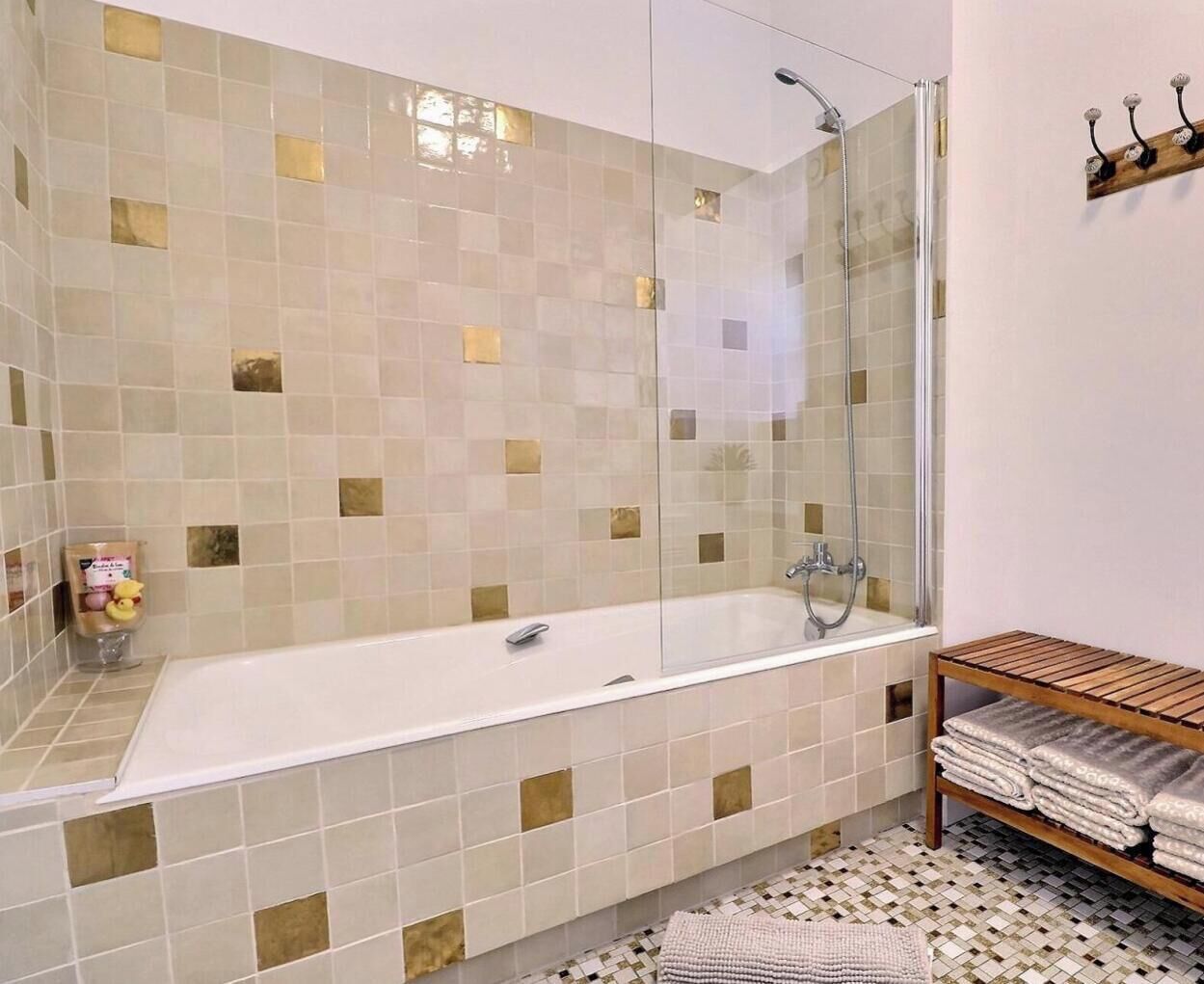 Un baño con ducha envuelta en vidrio, una bañera blanca y un estante de madera con toallas.