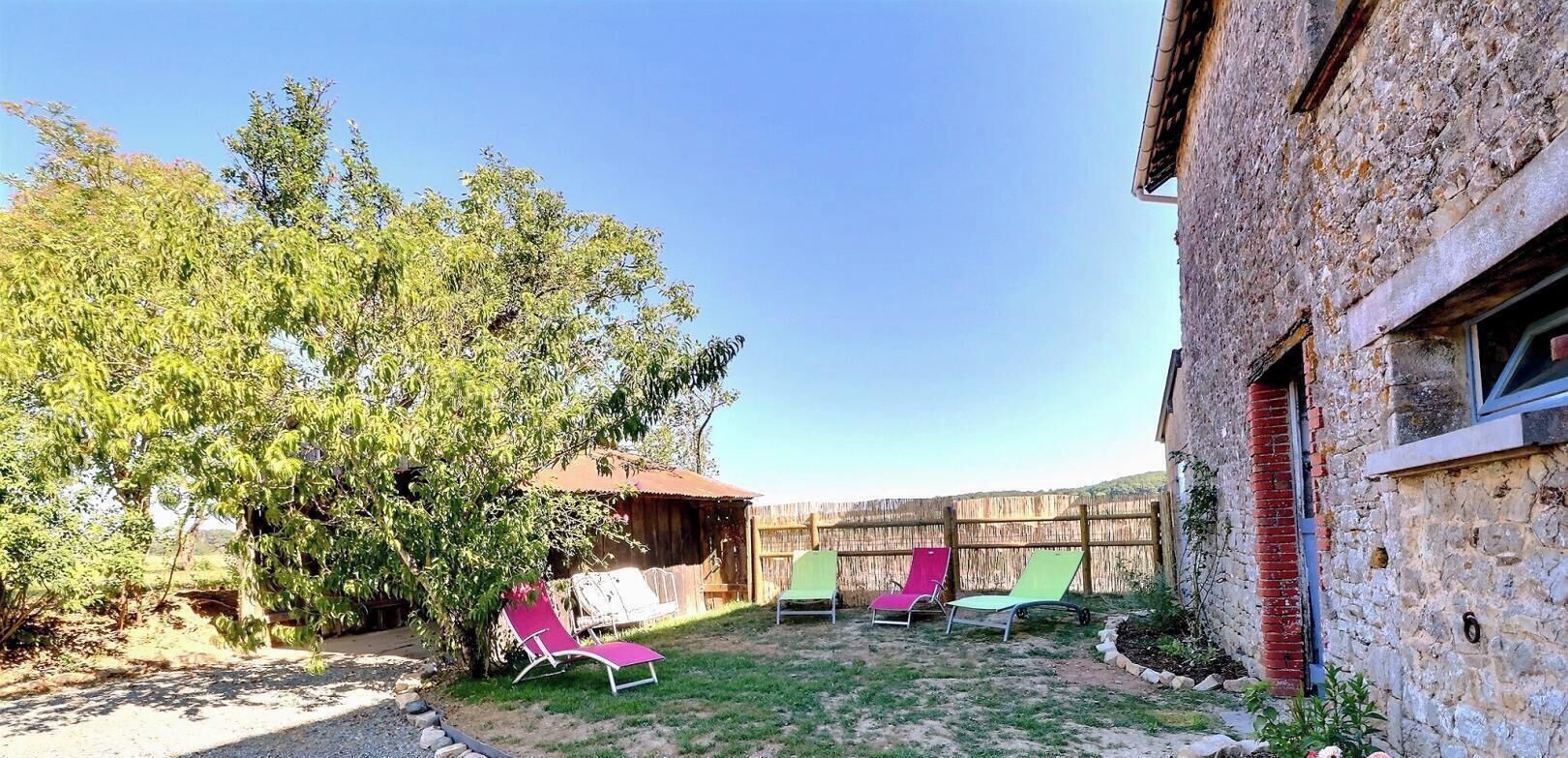 Un patio trasero con una valla de madera, un árbol y tres sillas de descanso.