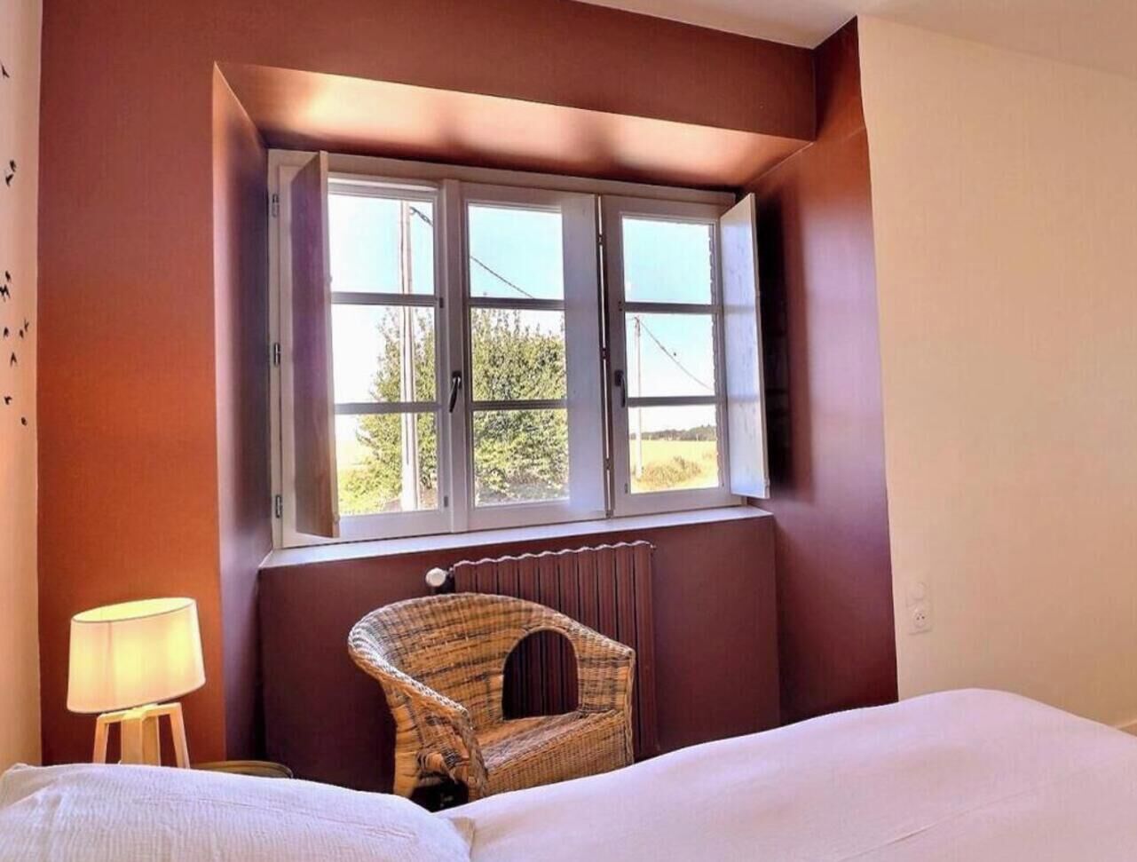 A bedroom with a bed, a chair, a window with a view, and a radiator.