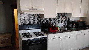 Une cuisine avec des meubles blancs, une cuisinière à gaz et un dosseret carrelé.
