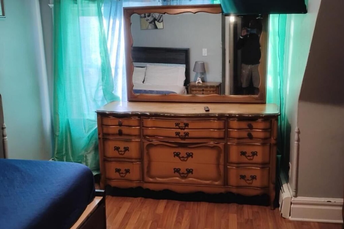 Un dormitorio con un aparador de madera, una cama con colcha azul y un espejo sobre el aparador.