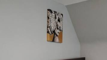 A bedroom with a bed, a nightstand with a lamp, a wall-mounted painting, and a wooden headboard.