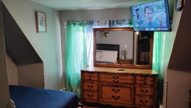Une chambre à coucher comprenant un lit, une commode, un miroir, une télévision et des rideaux.