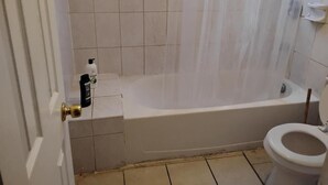 Une salle de bain avec une baignoire, des toilettes et une fenêtre avec des stores.