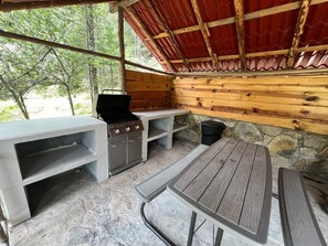Eine Terrasse im Freien mit Grill, Tisch und Bänken.