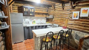 A rustic kitchen with a wooden ceiling, a tiled floor, a refrigerator, a sink, and a bar area with chairs.