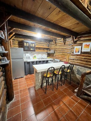 Une cuisine rustique avec un plafond en bois, un sol carrelé, un réfrigérateur, un évier et un coin bar avec des chaises.