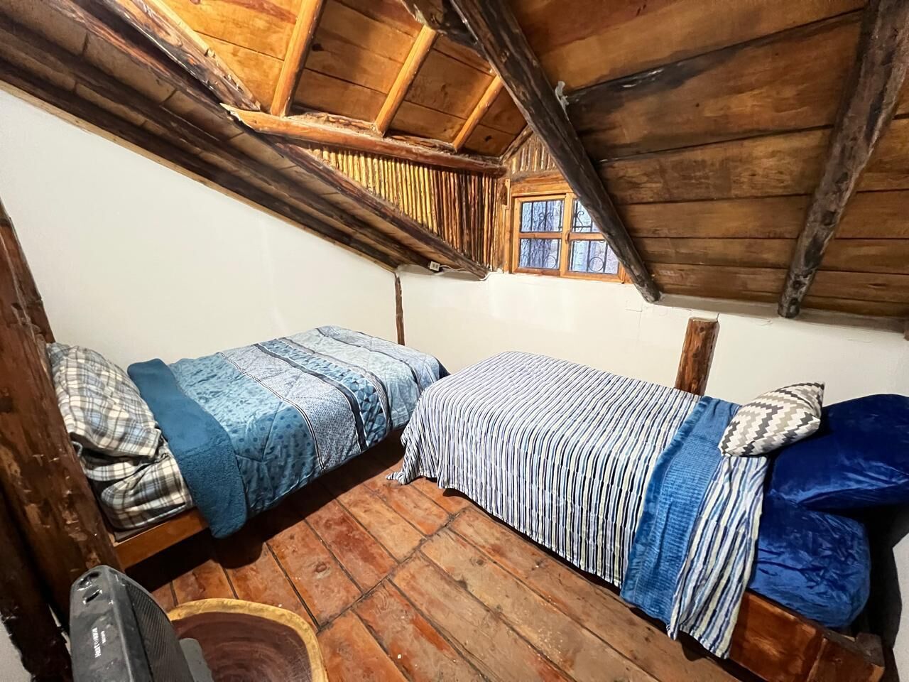 A small, rustic room with two wooden bunk beds, a wooden floor, and a window with a view.
