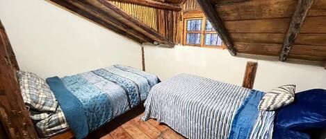 A small, rustic room with two wooden bunk beds, a wooden floor, and a window with a view.