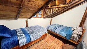 Two wooden bunk beds with blue bedding, a wooden floor, and a window with a metal grill.