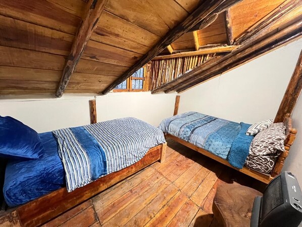 Two wooden bunk beds with blue bedding, a wooden floor, and a window with a metal grill.