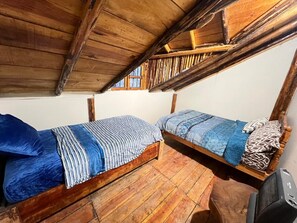 Deux lits superposés en bois, avec une literie bleue, un plancher en bois et une fenêtre munie d’une grille métallique.