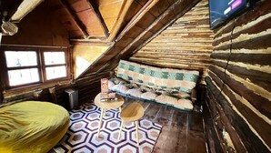 A cozy attic room with a sloped ceiling, a patterned rug, a sofa with cushions, and a small table with a book.