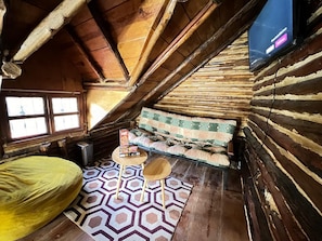 Une pièce mansardée chaleureuse, avec un plafond en pente, un tapis à motifs, un canapé avec des coussins et une petite table sur laquelle repose un livre.