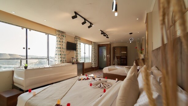 A hotel room with a large bed, a desk, a TV, and a view of the city. - Khofo Jacuzzi pyramids & GEM veiw (Giza Governorate)