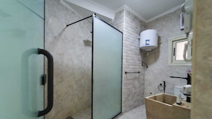 A bathroom with a glass shower enclosure, a white tiled wall, a white toilet, and a sink with a mirror. - Khofo Jacuzzi pyramids & GEM veiw (Giza Governorate)
