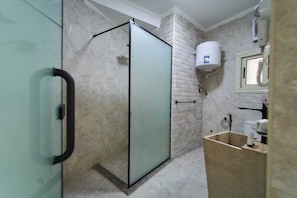 Ein Badezimmer mit Duschkabine aus Glas, einer weiß gefliesten Wand, einer weißen Toilette und einem Waschbecken mit Spiegel.