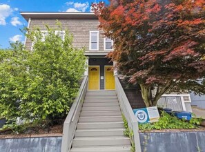 A staircase leading to a building with a yellow door, surrounded by greenery and a tree with red leaves. - Bright 2BR w/ Free Parking Near Downtown Seattle (Seattle)