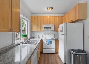 A compact kitchen with wooden cabinets, a stainless steel sink, a microwave, an oven, and a refrigerator. - Bright 2BR w/ Free Parking Near Downtown Seattle (Seattle)