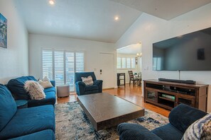 A living room with a sofa, armchair, coffee table, TV stand, and a dining area with a table and chairs. - The Blue Bungalow, Torrance CA (Torrance)