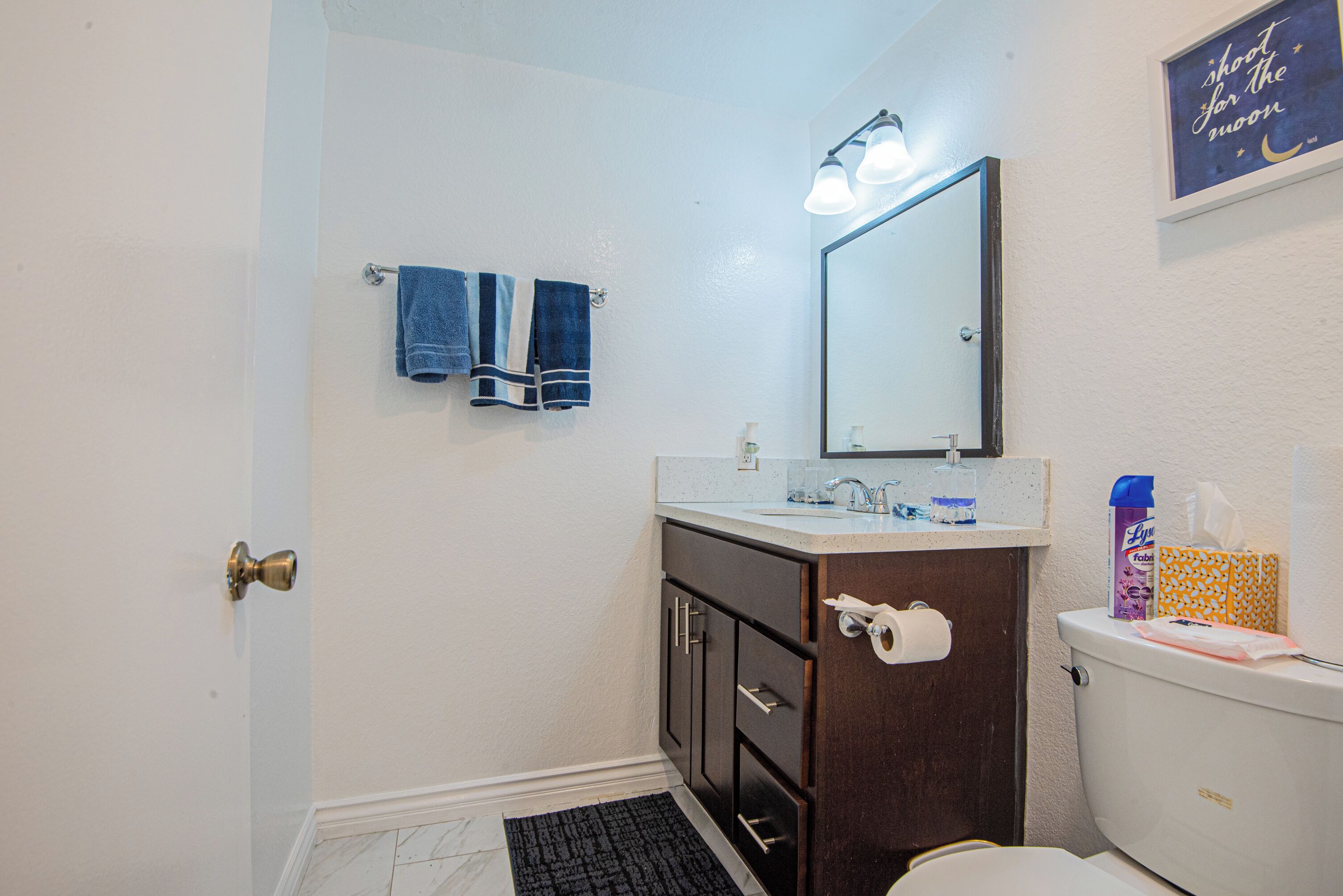 Une salle de bain comprenant des toilettes, un lavabo, un miroir, un porte-serviettes et une porte.