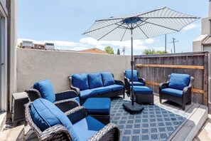 An outdoor patio with wicker furniture, a patterned umbrella, and a view of neighboring buildings. - The Blue Bungalow, Torrance CA (Torrance)