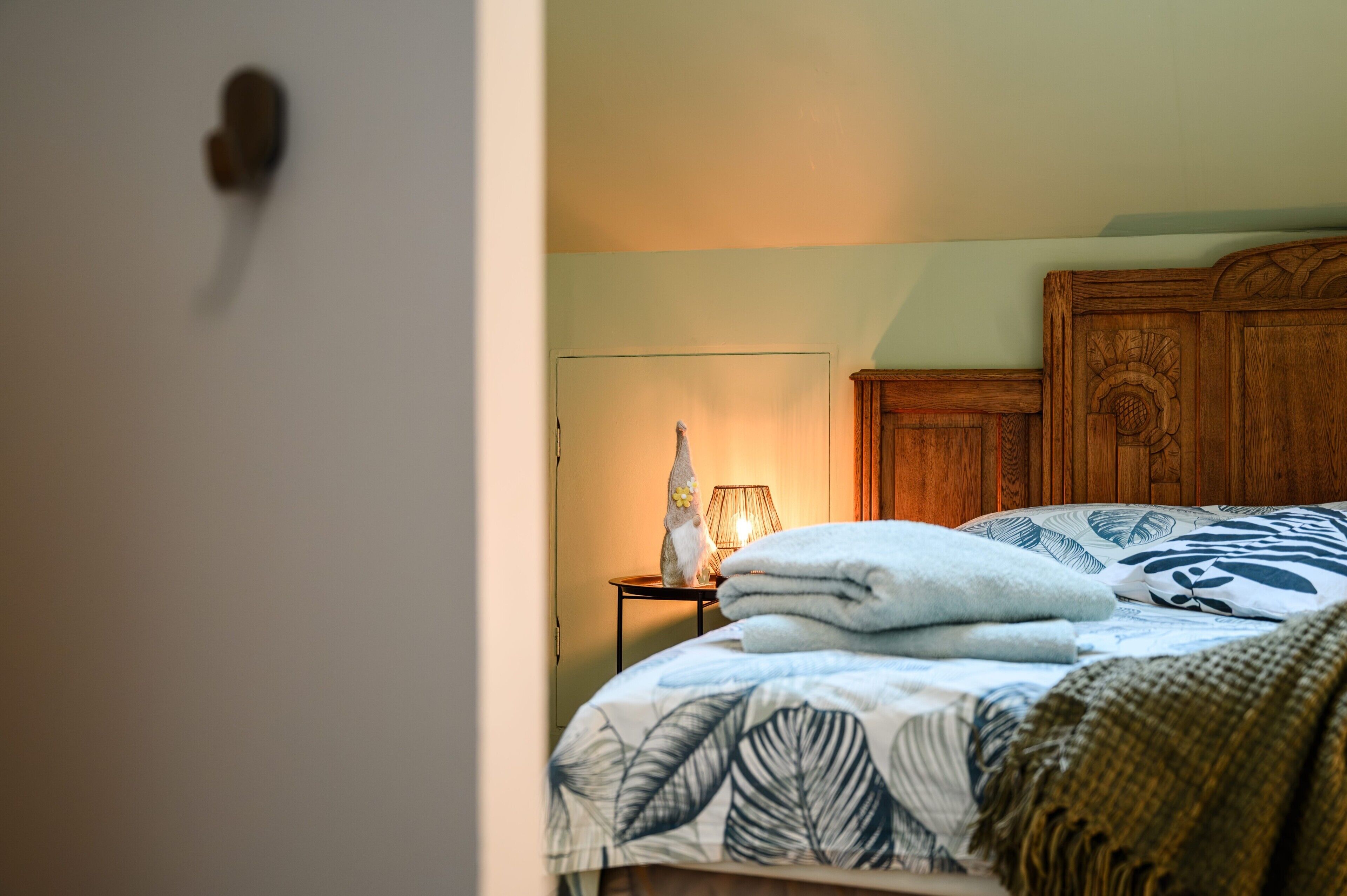 Een slaapkamer met een bed, nachtkastje, lamp en houten hoofdbord.